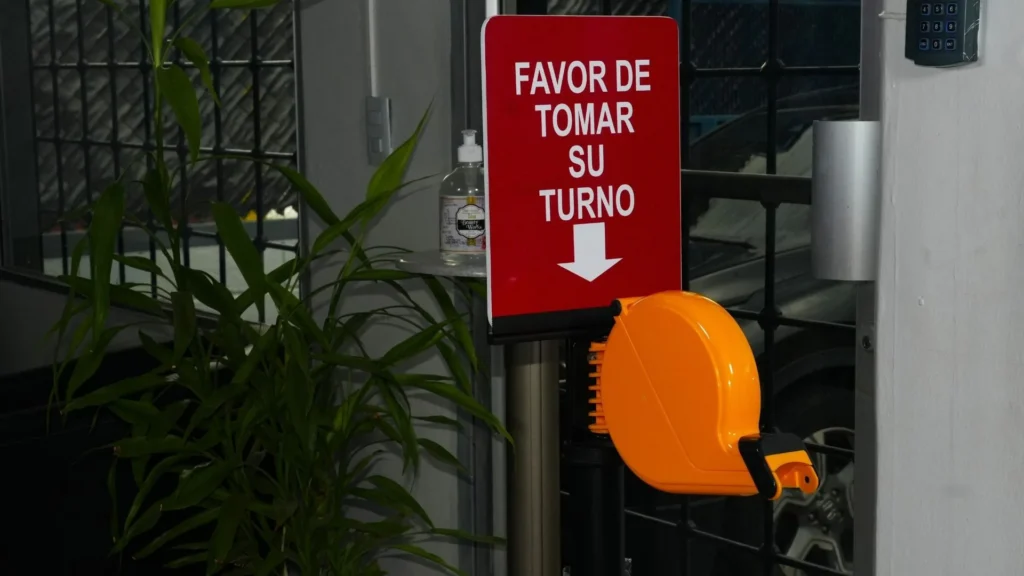 Dispensador naranja del kit toma turnos bajo el letrero rojo que pide tomar el turno.