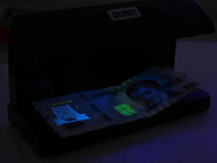 Lámpara UV Volteck 2 Lámpara UV Volteck encendida, con un billete de 100 lempiras en la base.
