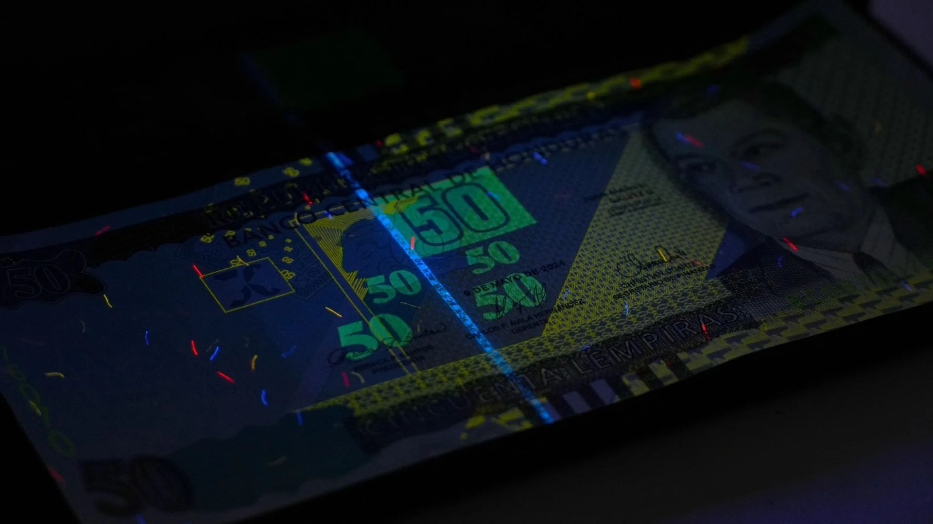 Billete de 50 lempiras bajo la luz ultravioleta, con sus fibras y marcas de seguridad fluorescentes.