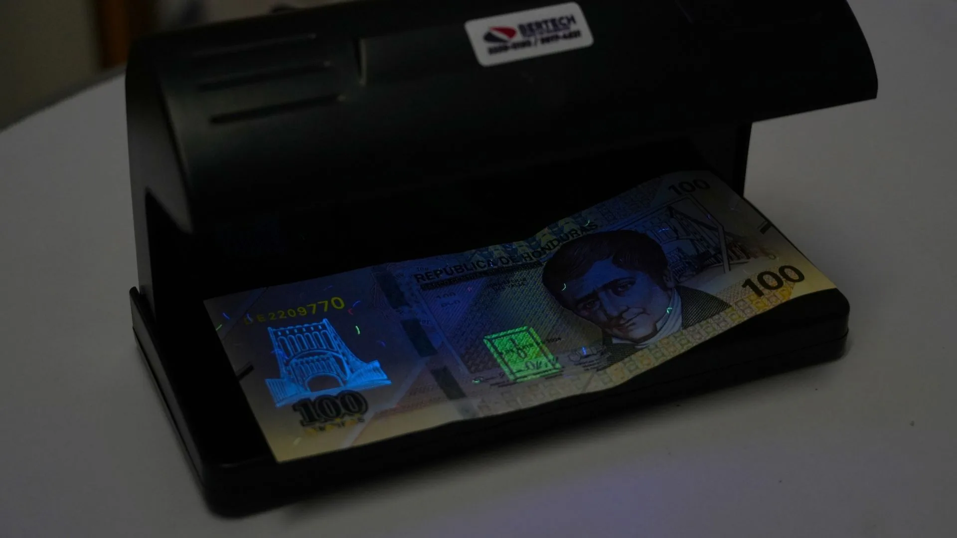 Billete de 100 lempiras revisado bajo la lámpara UV para detectar billetes falsos.