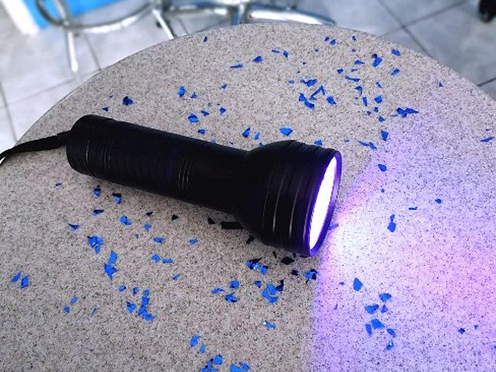 Linterna ultravioleta portátil encendida con su funda de transporte, proyectando luz UV sobre una superficie.