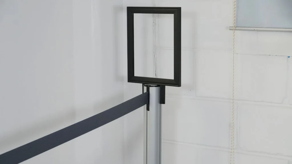 Porta letrero vertical para poste de fila, montado en un poste plateado con cinta negra.