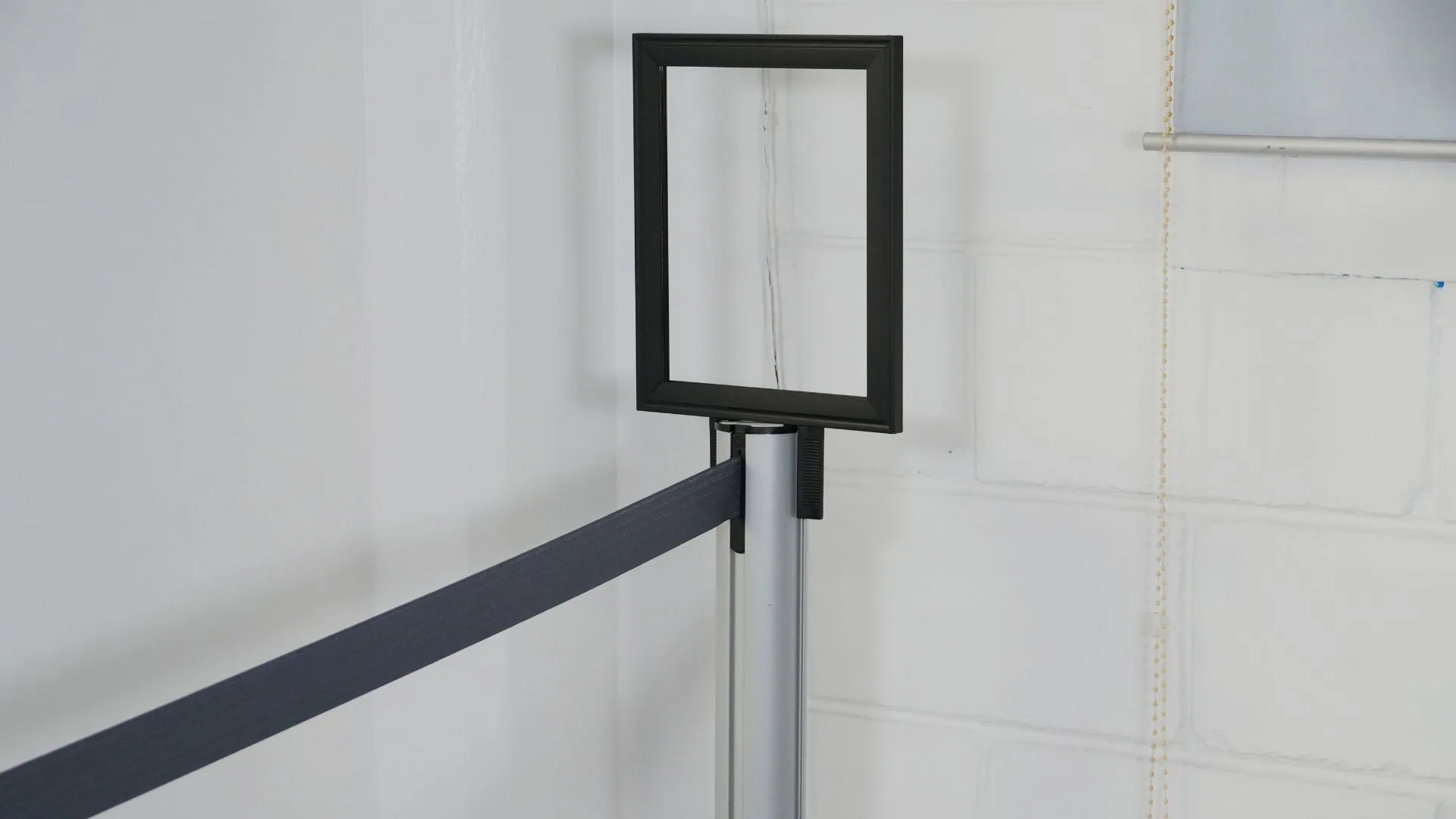 Porta letrero vertical para poste de fila, montado en un poste plateado con cinta negra.