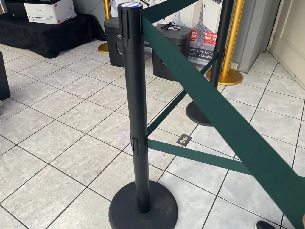 Poste de fila dual con sus dos cintas verdes cruzadas en diagonal hacia otros postes.