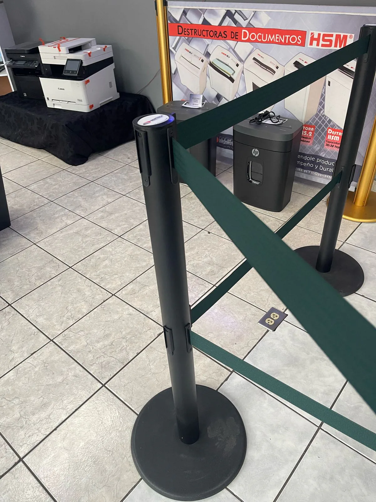 Poste de fila dual con sus dos cintas verdes tendidas en ángulo hacia otro poste.
