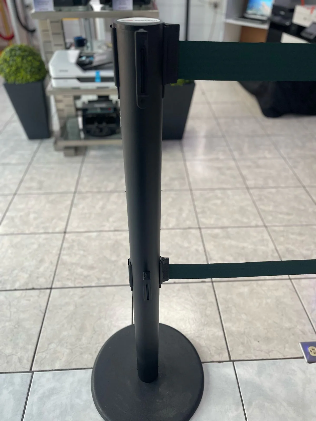 Poste de fila dual visto de cerca, con sus dos cintas verdes saliendo a distinta altura.