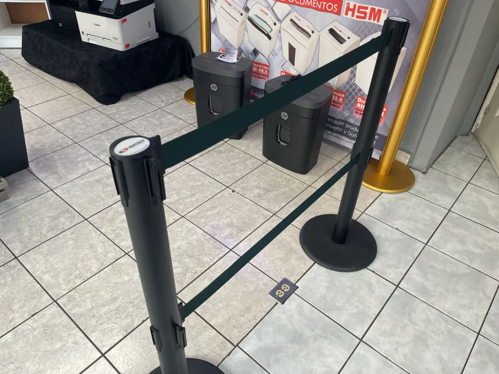 Dos postes de fila dual unidos por su doble cinta verde, frente a una exhibición de trituradoras.