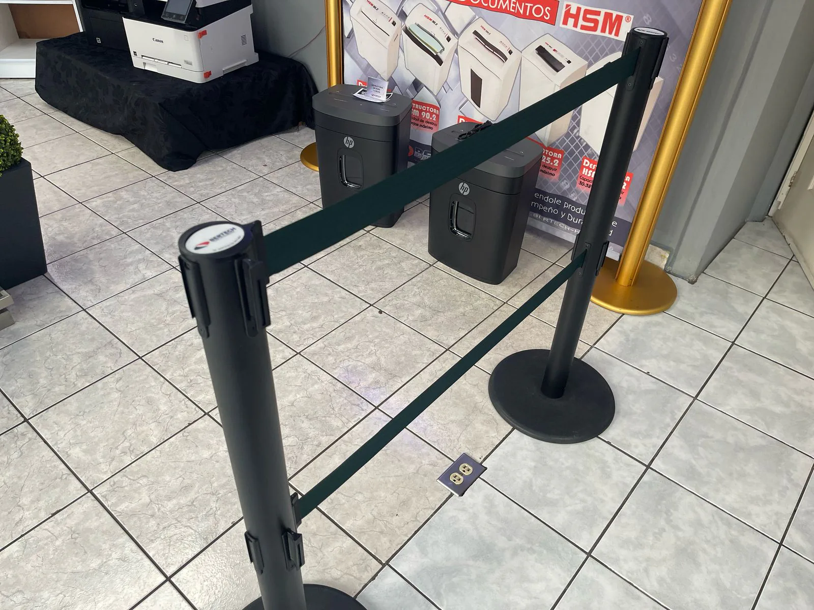 Dos postes de fila dual unidos por su doble cinta verde, frente a una exhibición de trituradoras.