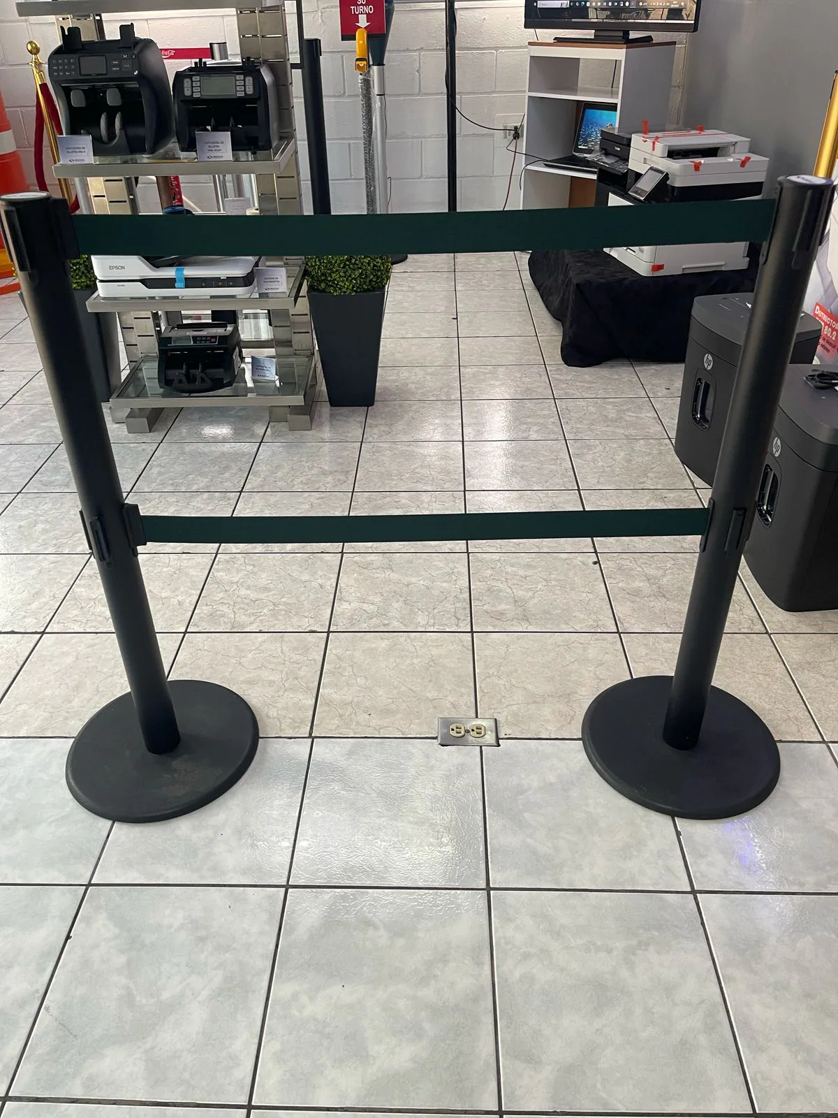 Dos postes de fila dual negros unidos por dos cintas verdes retráctiles, en la tienda de Bertech.