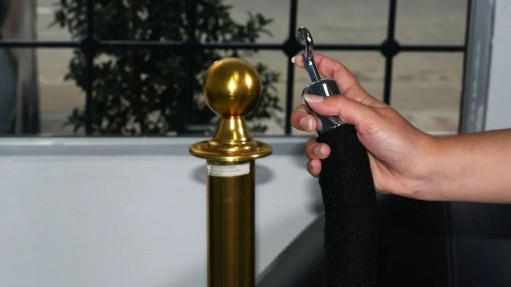 Mano enganchando el cordón de terciopelo negro en un poste de fila ejecutivo dorado.