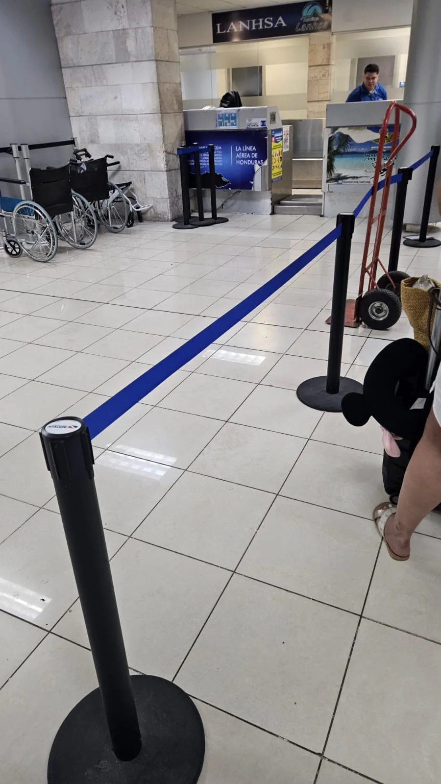 Poste de fila sencillo negro con cinta azul, frente al mostrador de una aerolínea en un aeropuerto.