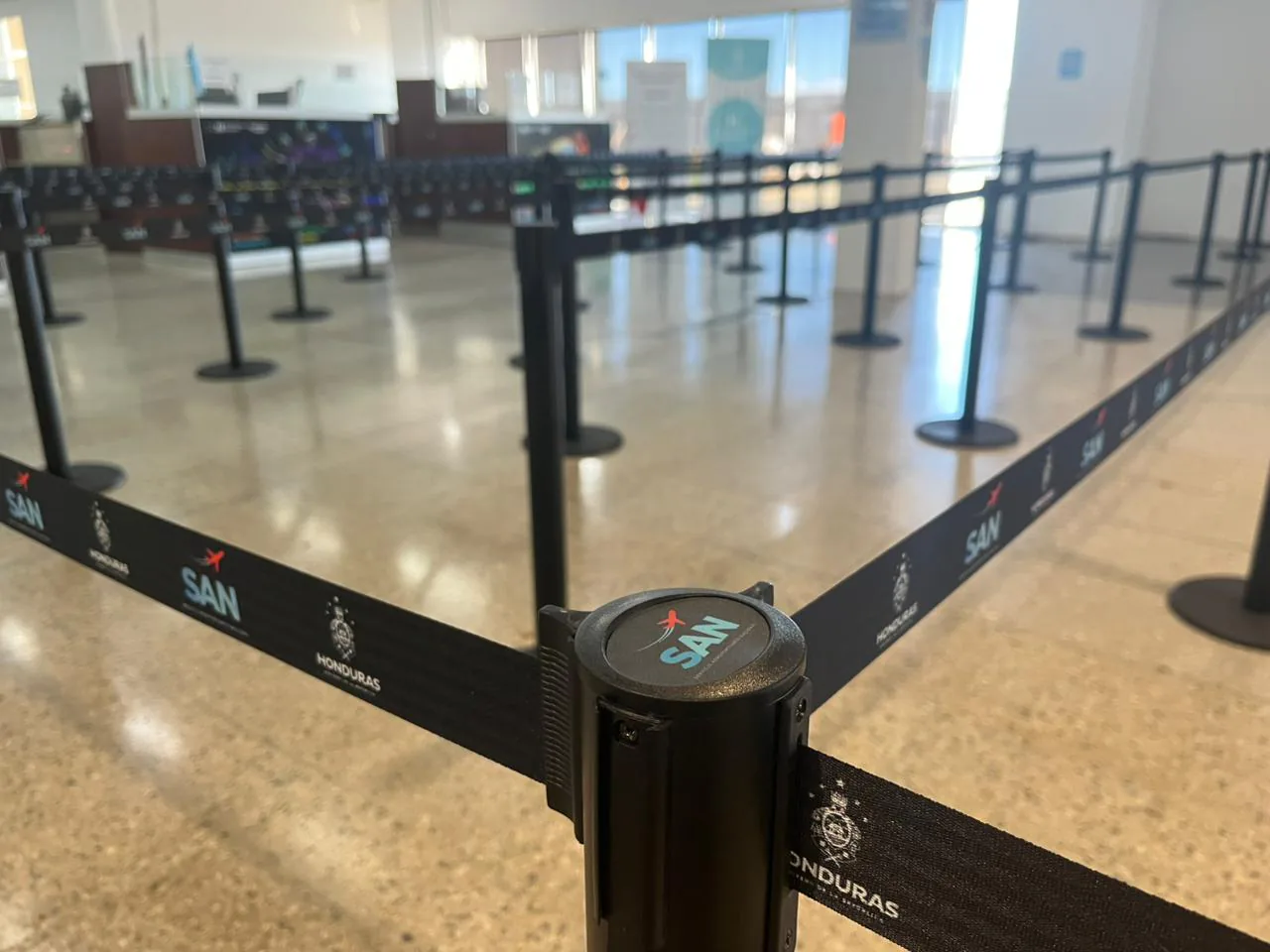 Cabezal de un poste separador de fila con el logotipo SAN y sus cintas impresas, en el aeropuerto de Roatán.