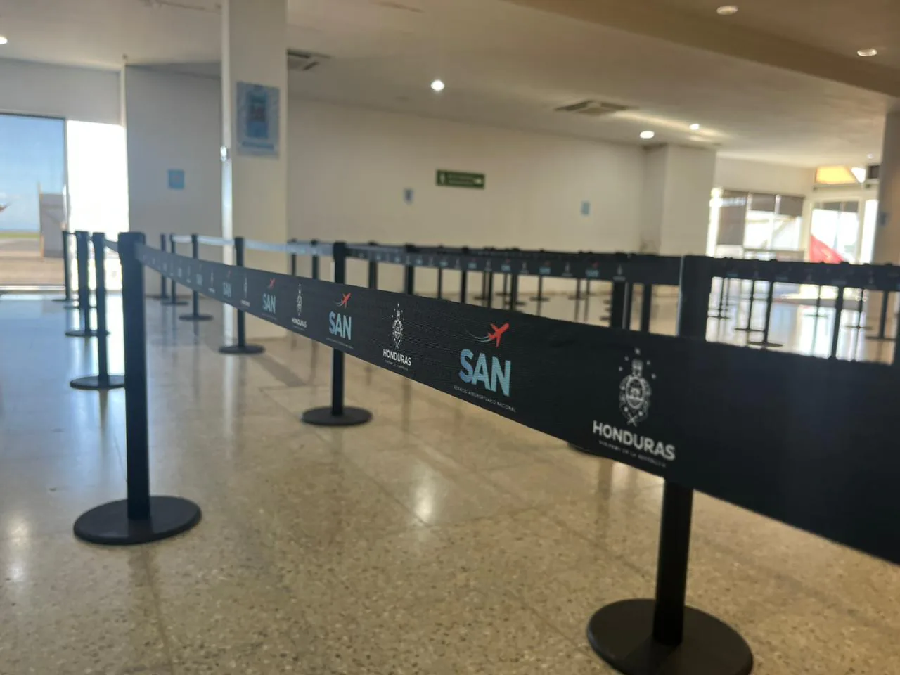 Cinta negra impresa con los logotipos SAN y Honduras en los postes separadores de fila del aeropuerto de Roatán.
