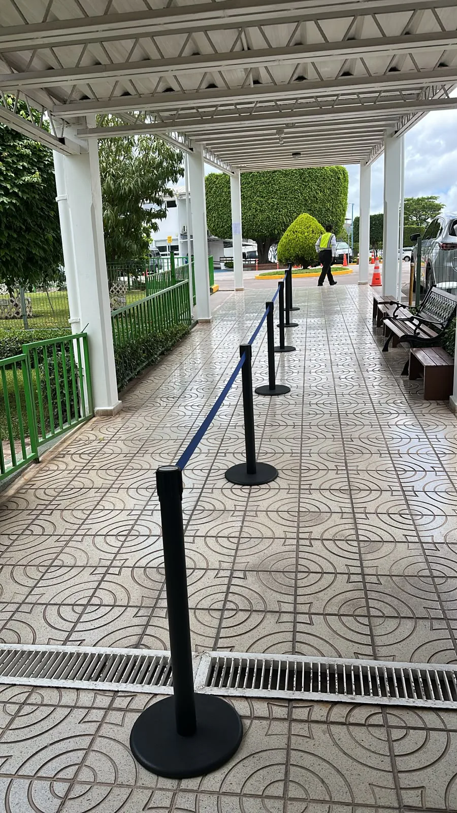 Postes separadores de fila con cinta azul a lo largo de un pasillo techado al aire libre.