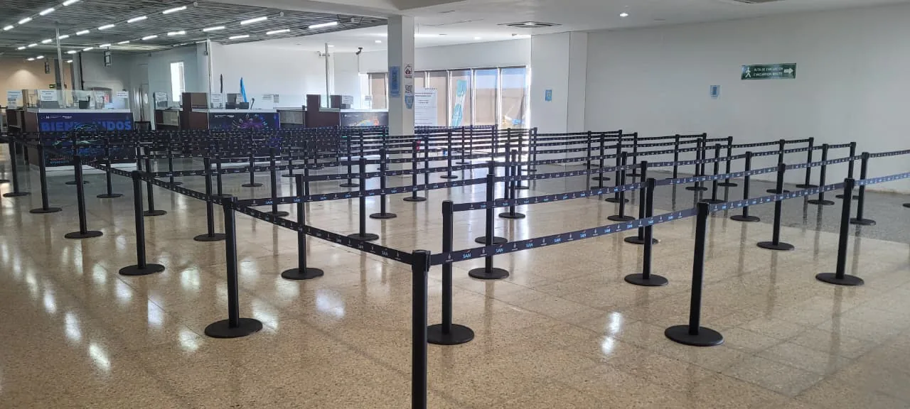 Filas en zigzag armadas con postes separadores frente a los mostradores del aeropuerto de Roatán.