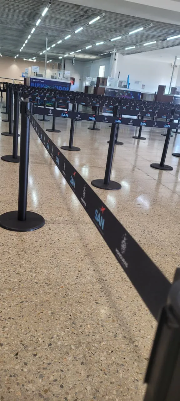 Hilera de postes separadores de fila con cinta impresa hacia los mostradores del aeropuerto de Roatán.