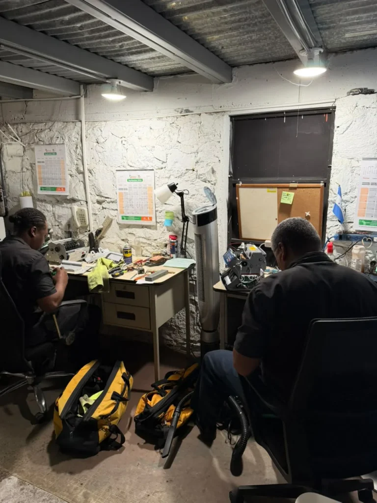 Mesas de trabajo del taller con dos técnicos y sus maletines de herramientas en el piso.