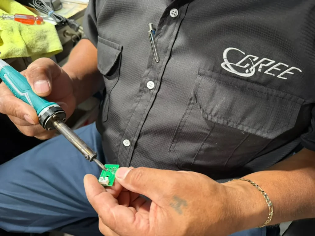 Técnico con el uniforme de CREE soldando una tarjeta electrónica con un cautín.