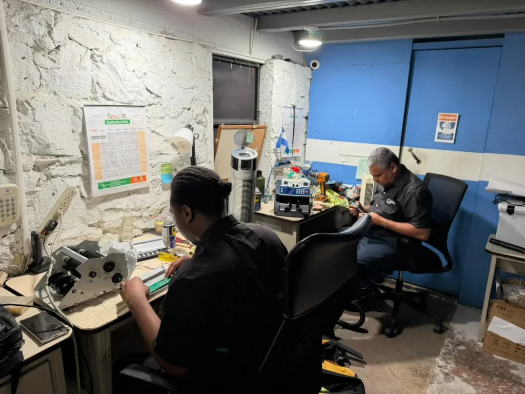 Vista del taller de reparación con dos técnicos trabajando en sus mesas.